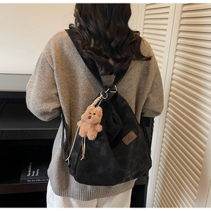 Detail of black vintage backpack with brown plush bear charm and leather logo patch