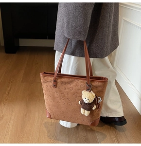Detail of brown suede tote bag with embossed bear pattern and plush bear charm