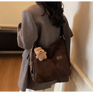Detail view of deep brown frosted leather tote with a cute plush bear accessory
