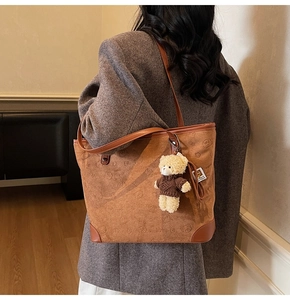 Close-up of vintage brown tote bag with bear patterns and plush bear charm on a shoulder