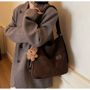 Detail of dark brown leather tote bag featuring a cute teddy bear plush charm