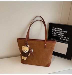 Close-up of brown suede tote bag featuring embossed bear patterns and a plush charm