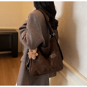 Detail of dark brown matte tote bag with teddy bear charm and brand logo patch