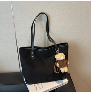 Close-up of black tote bag with silver rivets and cute plush bear charm on white books