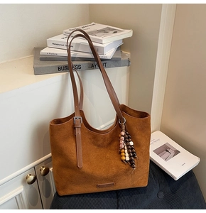Détail d'un grand sac cabas en daim marron avec bandoulière réglable et breloque perlée