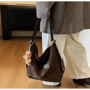 Side view of dark brown leather tote bag with plush bear charm and side pocket