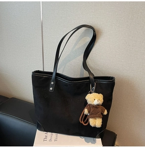 Detail of black tote bag material with embossed texture and cute plush bear charm