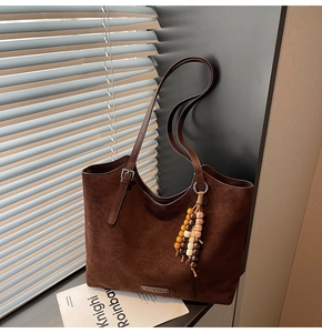 Détail d'un cabas en daim marron foncé avec pendentif en perles et boucle argentée