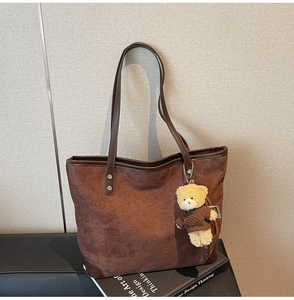 Detail shot of a large brown tote bag with cartoon embossing and a cute teddy bear charm