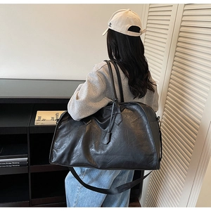 Détail d'un sac cabas en cuir noir avec de larges anses et une texture souple plissée