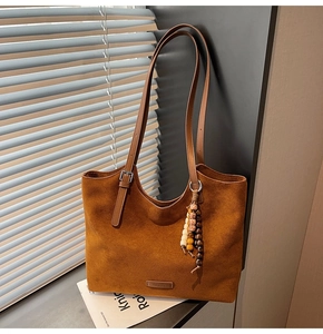 Détail d'un sac cabas en daim marron avec breloque en perles de bois et logo embossé