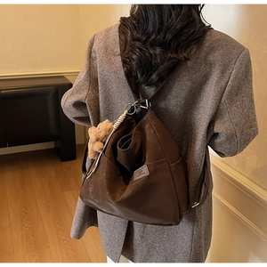 Detail of dark brown tote bag featuring a leather logo patch and cute plush bear charm