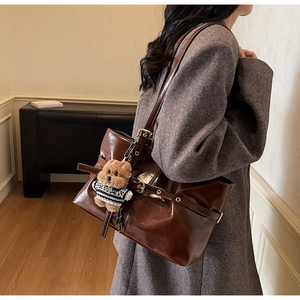 Détail du cabas en cuir ciré marron foncé avec boucle et breloque ours sur le mannequin