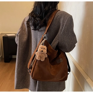 Detail view of large dark brown leather hobo bag with a plush teddy bear charm accessory