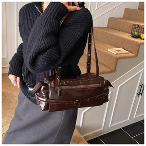 Detail of dark brown glossy patent leather Boston bag with decorative buckle and long strap