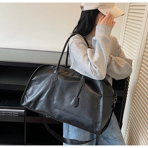 Détail d'un grand sac cabas vintage en cuir noir avec bandoulière réglable et poignée chic