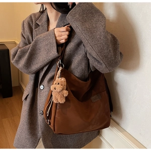 Detail view of large brown hobo bag with plush puppy charm and woven fashion label