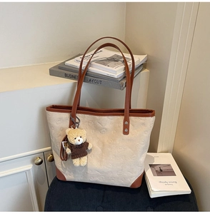 Close-up of beige canvas tote bag with brown leather handles and cute bear charm