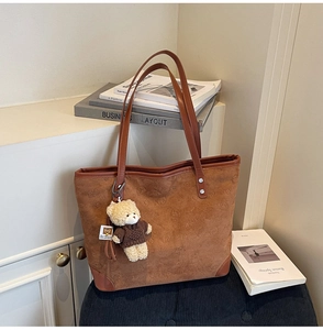 Close-up of brown suede tote bag with embossed bear pattern and cute plush bear charm