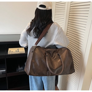 Modèle portant un grand sac de voyage marron foncé avec bandoulière et fini rétro