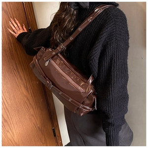 Detail of dark brown glossy shoulder bag with silver eyelets and buckle straps