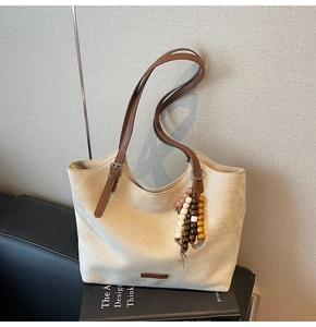 Détail du sac cabas en daim avec bandoulières en cuir marron et pompon en perles de bois