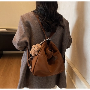 Detail of brown vintage leather backpack with plush bear charm and embossed logo