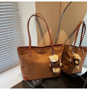 Detail of brown suede tote bag with embossed bear pattern and cute plush charm pendant