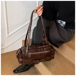 Detail of dark brown glossy underarm bag with multi-zipper pockets and metallic eyelet straps