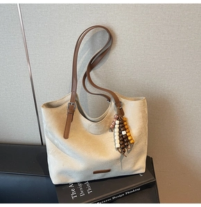 Détail du cabas beige avec bandoulières marron et charms en perles de bois sur livre