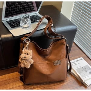 Detail of a dark brown tote bag with twin front pockets and a plush bear charm detail