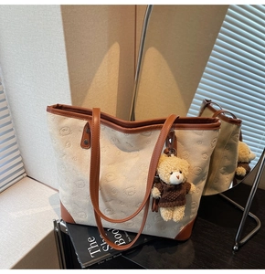 Detail of cream tote bag with embossed bear pattern and brown leather straps on a desk