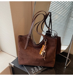 Détail d'un sac cabas en daim marron avec un pompon en perles colorées et boucle en métal