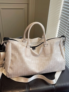 Large white woven travel bag with herringbone texture and detachable shoulder strap on a bench