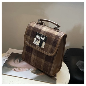 Détail du sac vintage en tweed à carreaux marron avec écusson ours sur un bureau