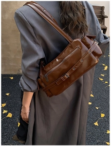 Close-up of dark brown patent leather shoulder bag with metallic eyelets and zipper