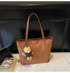 Detail view of brown suede tote bag with bear embossing and plush bear charm accessory