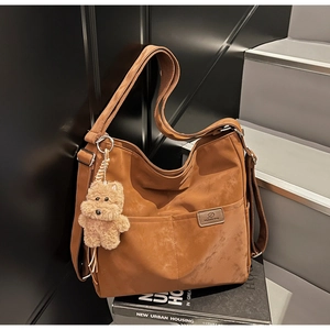 Detailed texture of brown suede tote bag with adjustable strap and teddy bear charm