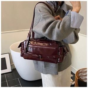 Detail of burgundy patent leather cylinder shoulder bag with silver hardware and buckles