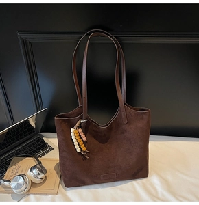Détail du grand sac cabas en daim marron avec pendentif en perles colorées sur un lit blanc