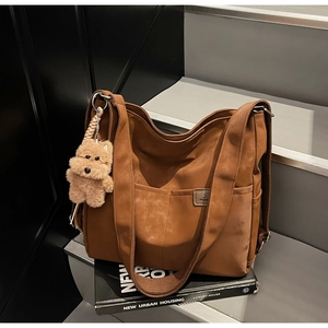 Brown nylon tote bag on stairs with a teddy bear charm and wide shoulder strap