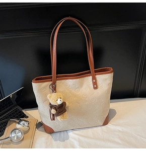 Detailed close-up of a large tote bag with bear patterns, leather handles, and a plush charm