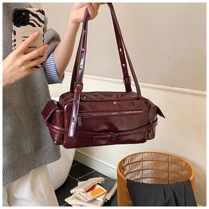 Detail of burgundy glossy leather shoulder bag with metallic eyelets and buckle straps