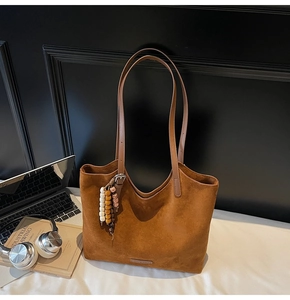 Détail d'un sac cabas en daim marron avec pompon bohème dans un décor de bureau moderne