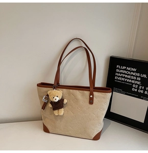 Close-up of beige tote bag with embossed bear patterns and a cute plush bear charm