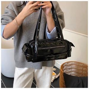 Detailed close-up of a black patent leather shoulder bag with decorative buckles and zippers
