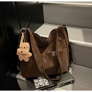Detail of vintage brown tote bag with plush bear charm on urban bookshelf