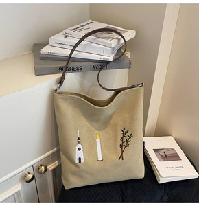 Close-up of beige canvas tote bag featuring minimalist embroidery and brown leather strap
