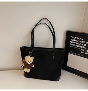 Detail of black suede tote bag with cute plush bear pendant and reinforced corners