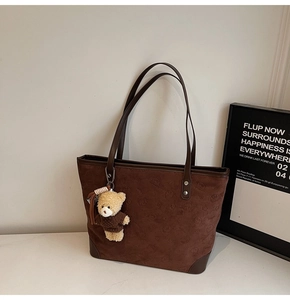 Detail view of dark brown tote bag featuring embossed patterns and a cute bear charm